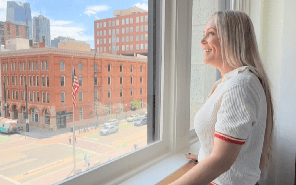 Erin Thorburn looks out a guestroom window at The Crawford Hotel overlooking downtown Denver and historic Union Station.