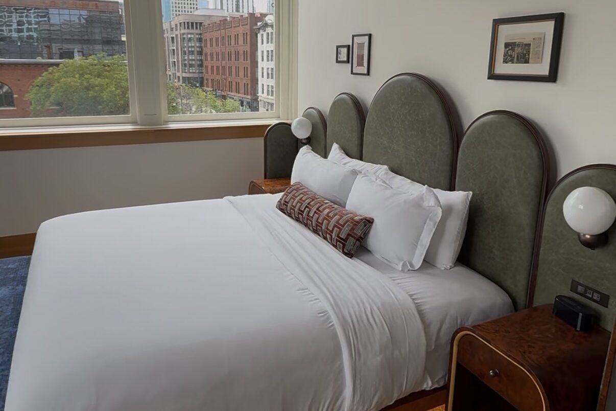 Spacious king guestroom at The Crawford Hotel with floral wallpaper ceiling, large windows, workspace and downtown Denver views.