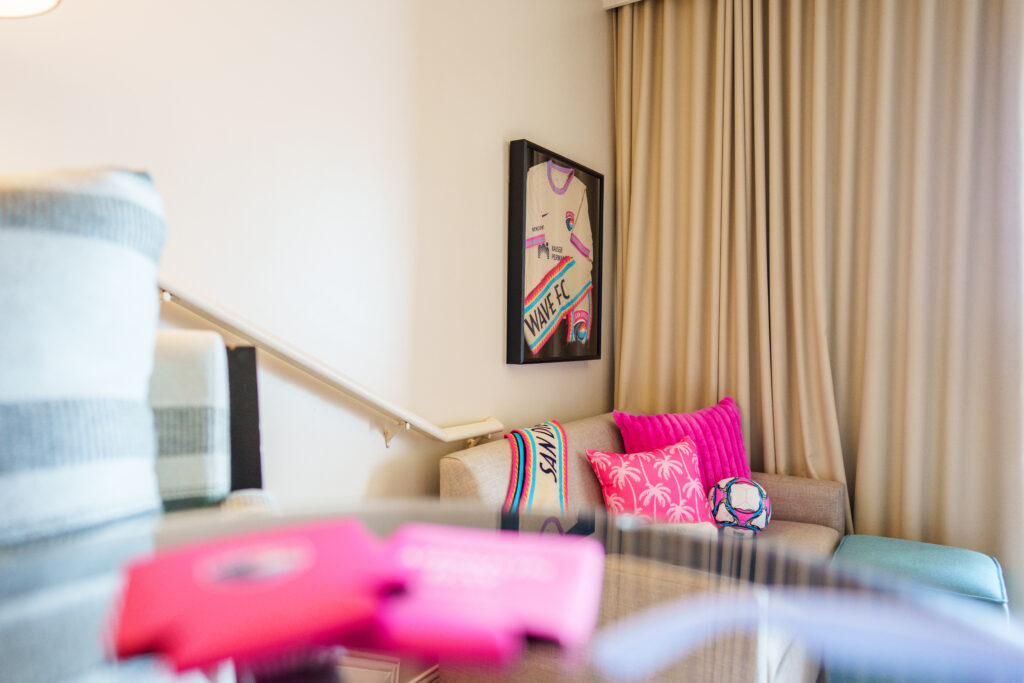 Living room inside the San Diego Wave FC Suite featuring team artwork, colorful pillows and soccer-themed décor.