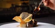 A plated dish at Atria in Flagstaff features wagyu, potato pavé and delicate garnishes as sauce is spooned over the dish.
