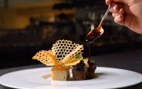 A plated dish at Atria in Flagstaff features wagyu, potato pavé and delicate garnishes as sauce is spooned over the dish.