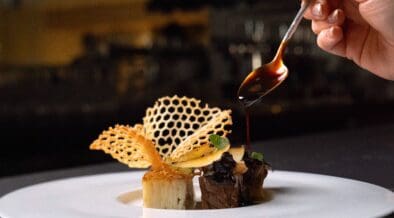 A plated dish at Atria in Flagstaff features wagyu, potato pavé and delicate garnishes as sauce is spooned over the dish.