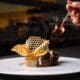 A plated dish at Atria in Flagstaff features wagyu, potato pavé and delicate garnishes as sauce is spooned over the dish.