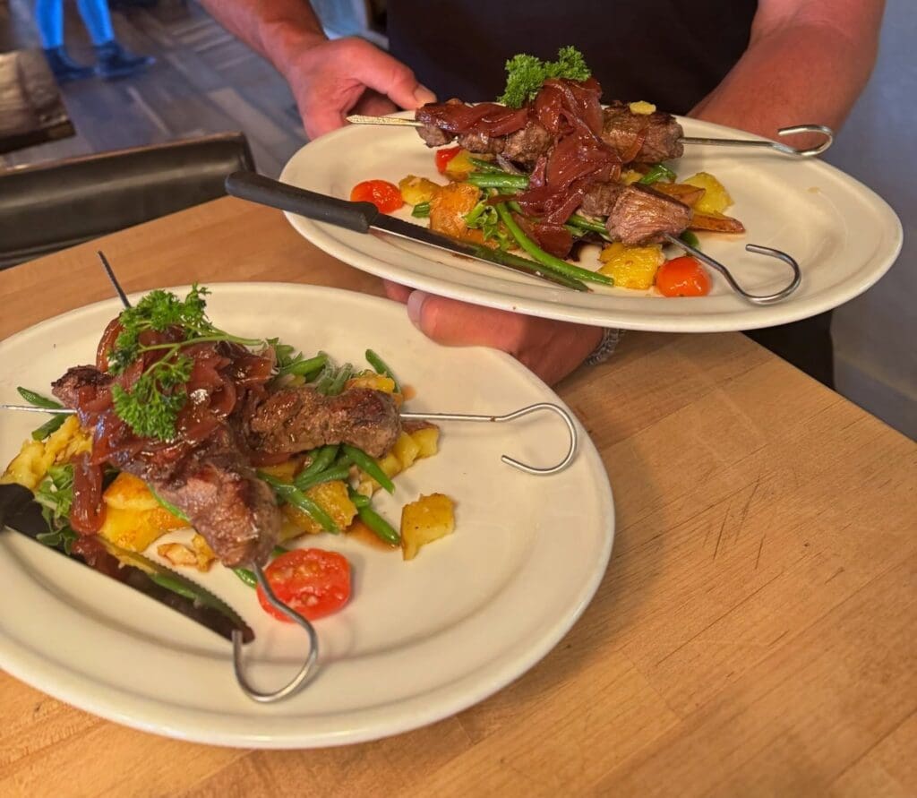 Two plates at Jambo Cafe in Santa Fe feature grilled meat skewers served with potatoes, green beans, tomatoes and greens.