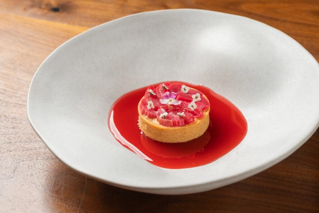 A colorful plated dish at Monte in South Salt Lake features a golden tart topped with vibrant red vegetables, edible flowers and a vivid red sauce.