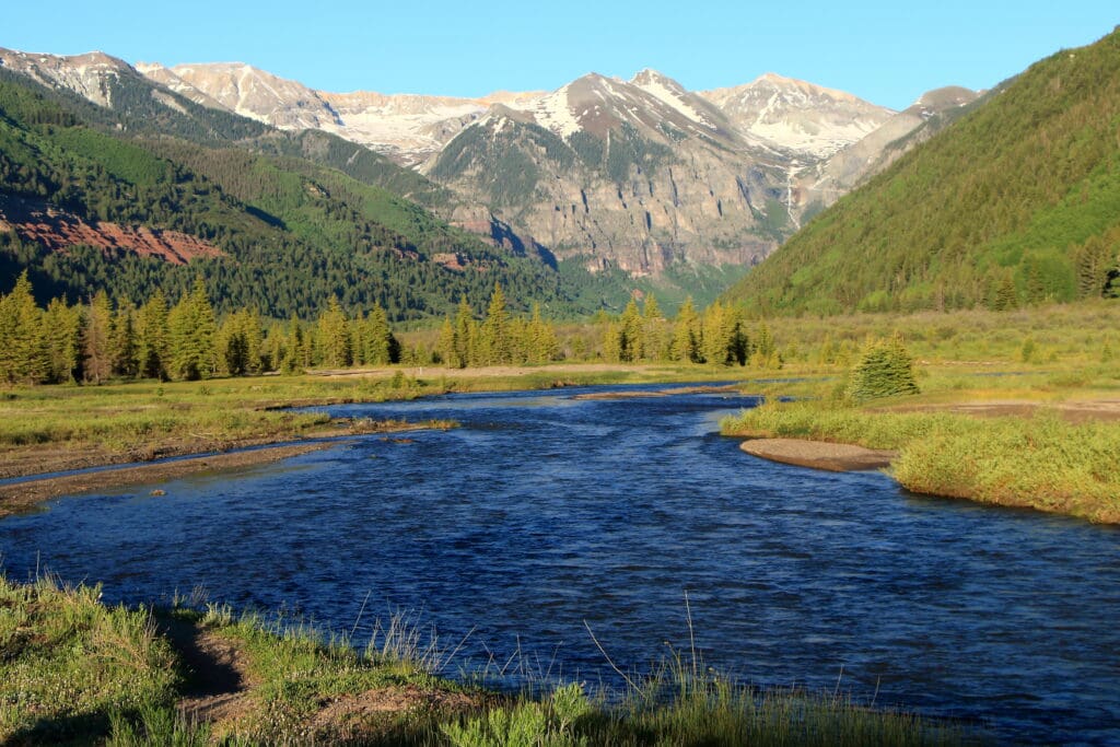 River flowing through a green mountain valley beneath snow-dusted peaks near Telluride, Colorado.
