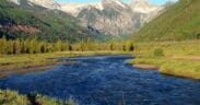River flowing through a green mountain valley beneath snow-dusted peaks near Telluride, Colorado.