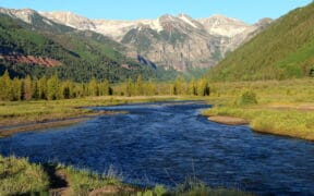 River flowing through a green mountain valley beneath snow-dusted peaks near Telluride, Colorado.