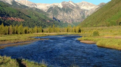 River flowing through a green mountain valley beneath snow-dusted peaks near Telluride, Colorado.