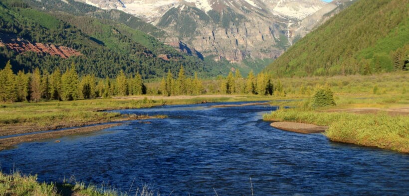 River flowing through a green mountain valley beneath snow-dusted peaks near Telluride, Colorado.