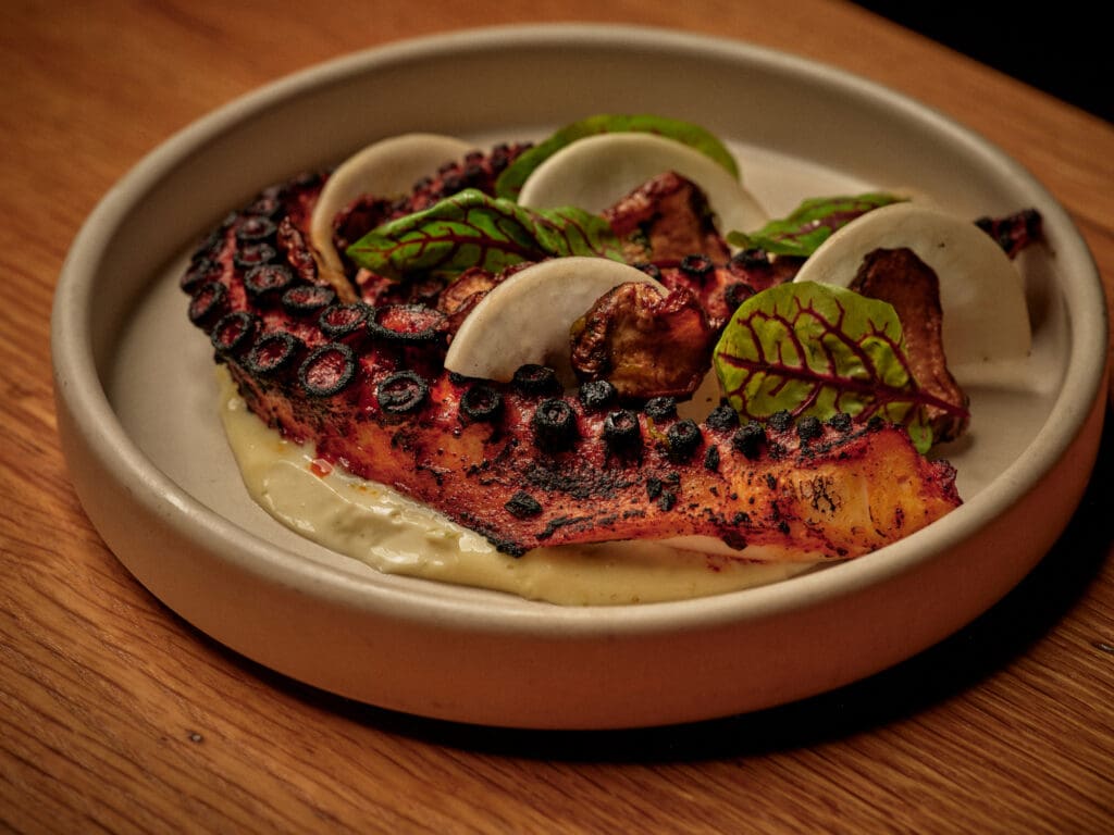 Charred octopus at Valentine in Phoenix is plated with sauce, sliced vegetables and leafy greens.