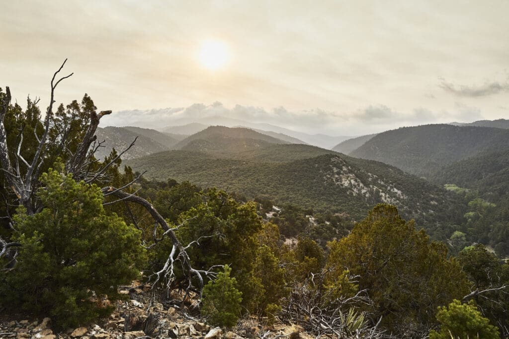 Sunlight over layered mountain ridges and juniper-covered high-desert terrain near Bishop’s Lodge in Santa Fe, New Mexico.