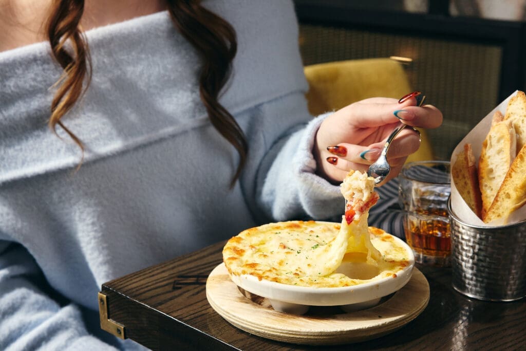 Guest lifting a spoonful of cheesy seafood dip at Harry & Izzy's restaurant.