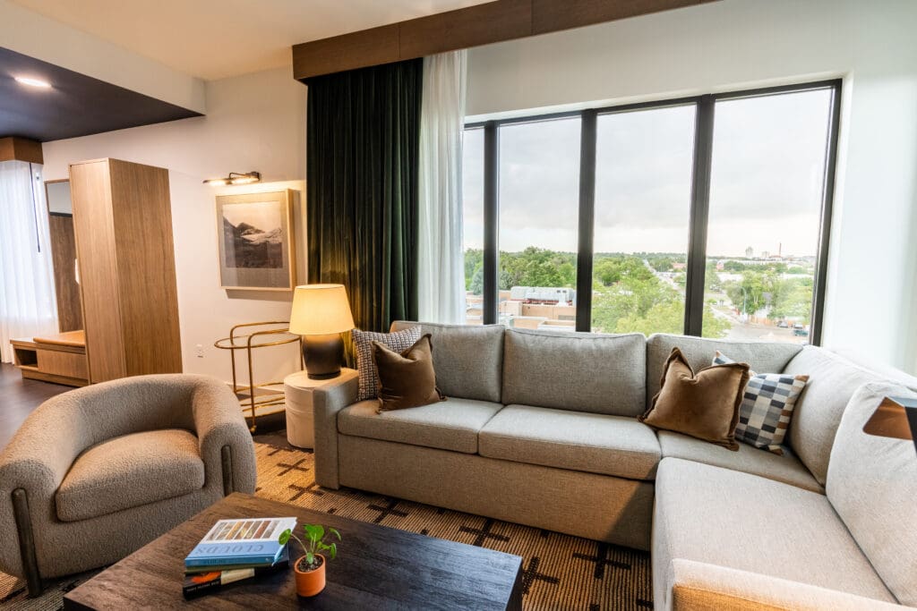 Modern guest suite at Hotel Longmont featuring a large sectional sofa, oversized windows and views of downtown Longmont.