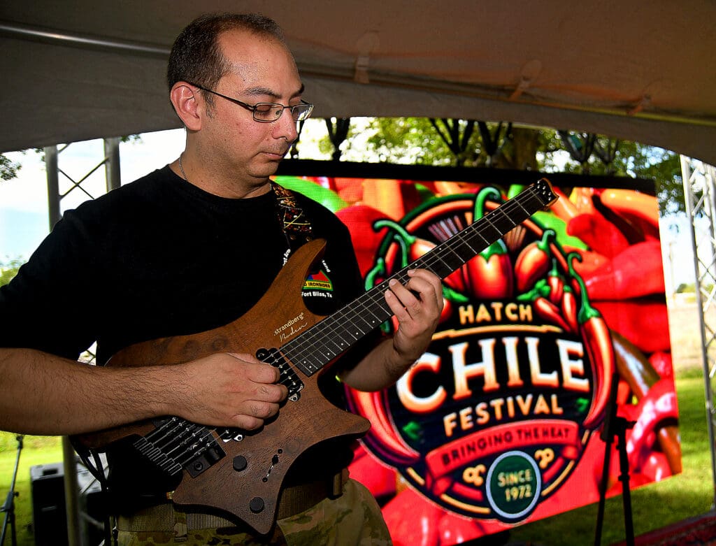 A man plays an electric guitar with the Las Cruces Hatch Chile Festival Logo sign in the background.
