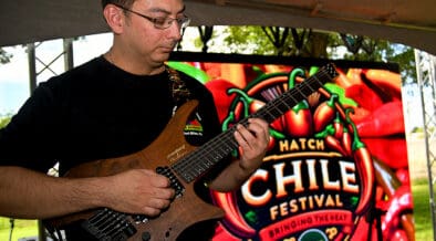 A man plays an electric guitar with the Las Cruces Hatch Chile Festival Logo sign in the background.