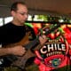 A man plays an electric guitar with the Las Cruces Hatch Chile Festival Logo sign in the background.