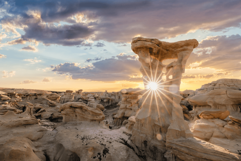 Sun shines through a sculpted sandstone formation amid the badlands of northwestern New Mexico at sunset.