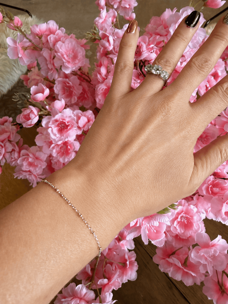 A permanent silver bracelet on a woman's wrist with pink cherry blossoms in the background at Chained Up in Denver.