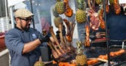 Chef preparing a large rack of meat alongside grilled cuts and pineapples at a previous RARE Steak Championship.