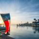 Texas flag overlooking Laguna Madre Bay at sunset on South Padre Island with boats, docks and palm trees in the distance.