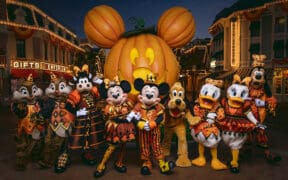 Mickey Mouse and friends in Halloween costumes pose in front of the giant Mickey pumpkin at Disneyland Resort.