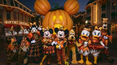 Mickey Mouse and friends in Halloween costumes pose in front of the giant Mickey pumpkin at Disneyland Resort.