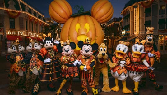 Mickey Mouse and friends in Halloween costumes pose in front of the giant Mickey pumpkin at Disneyland Resort.