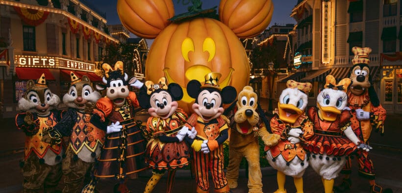 Mickey Mouse and friends in Halloween costumes pose in front of the giant Mickey pumpkin at Disneyland Resort.