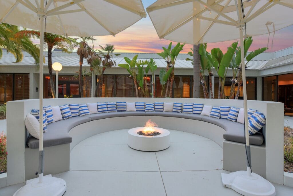 Circular outdoor lounge with a fire pit, umbrellas and tropical landscaping at Hilton Irvine.