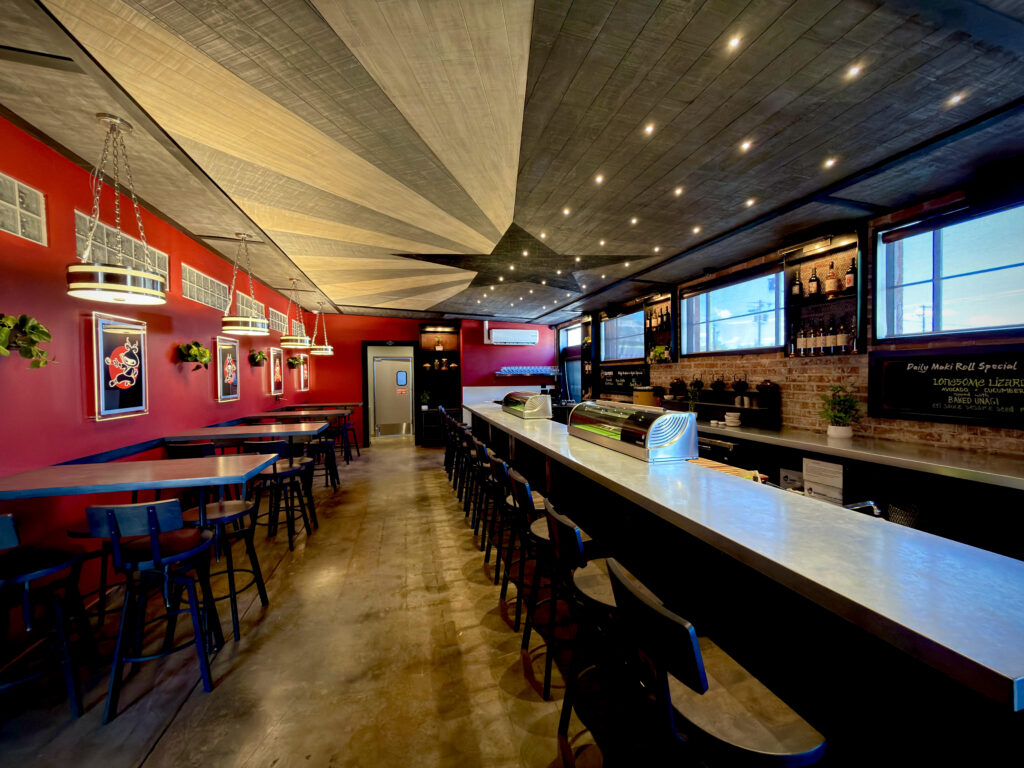 Interior of Queen B Sushi in Cottonwood with a long sushi counter, red walls and dining tables.