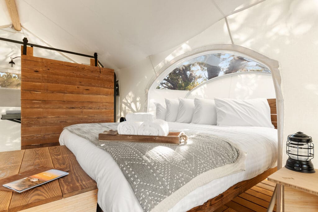 King-size bed positioned beneath a curved viewing window inside an Under Canvas Stargazer tent
