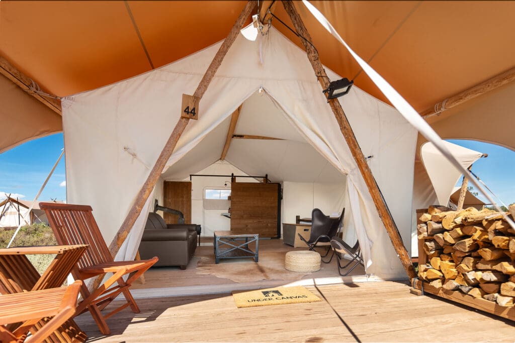 Open Under Canvas safari-style tent with a private deck, lounge furniture and stacked firewood
