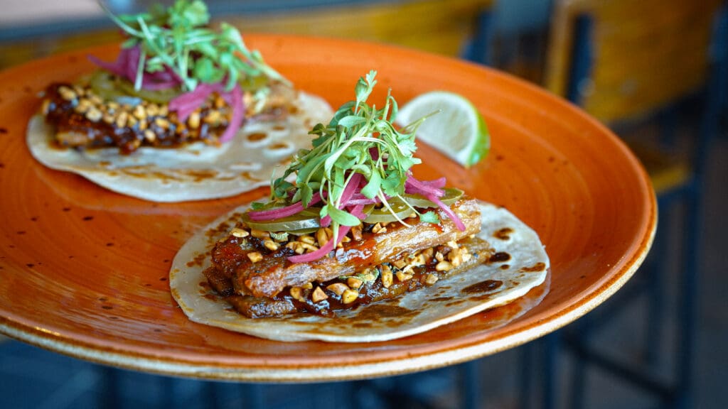 Duroc pork belly tacos topped with pickled vegetables, herbs and chopped nuts at Vecina.