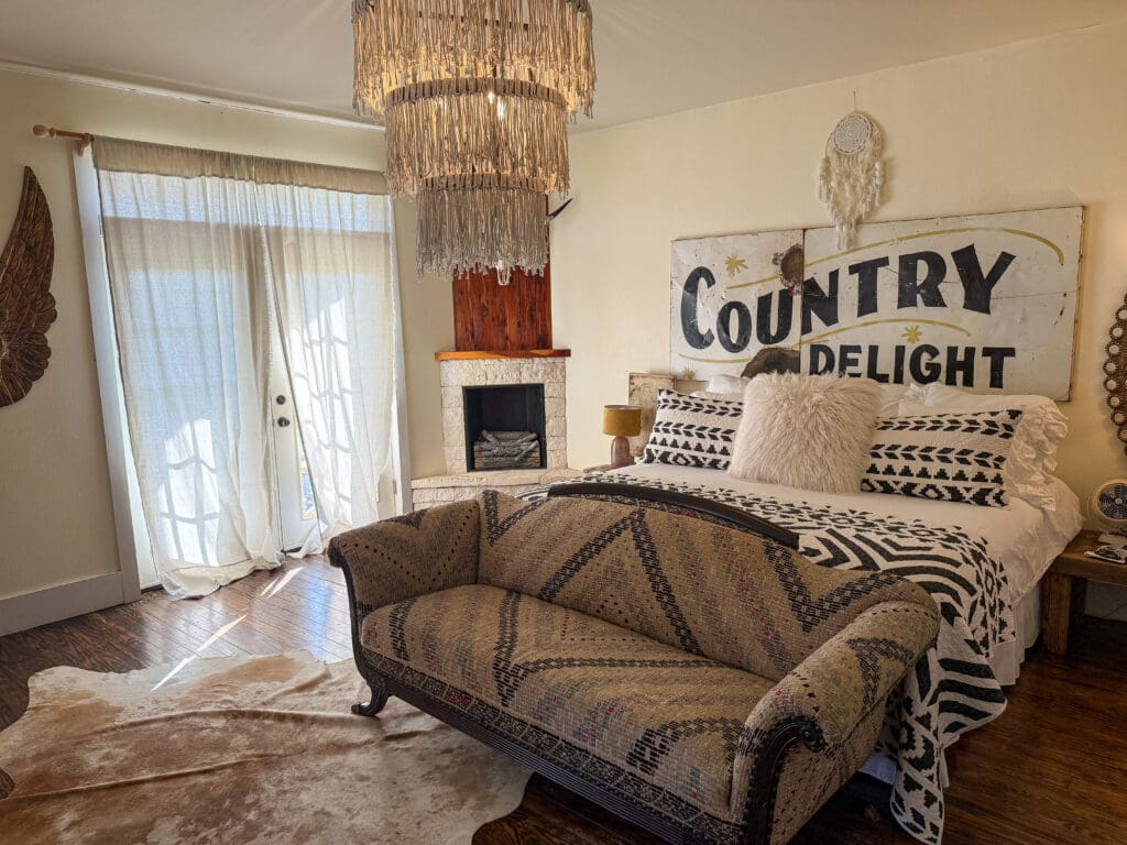 Guest room at Wander Inn in Round Top with black-and-white bedding, a vintage Country Delight sign, fireplace and patterned sofa.