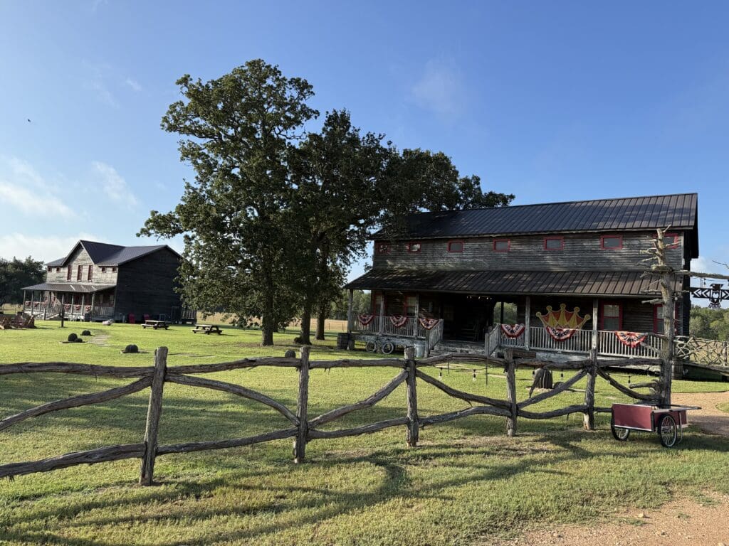 Rustic guest buildings, split-rail fencing and green lawn at Wander Inn in Round Top, Texas.