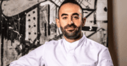 Chef Charbel Hayek wearing a white chef’s coat in front of black-and-white abstract artwork.