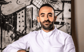 Chef Charbel Hayek wearing a white chef’s coat in front of black-and-white abstract artwork.