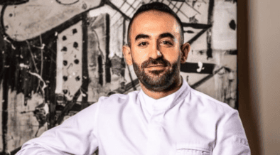 Chef Charbel Hayek wearing a white chef’s coat in front of black-and-white abstract artwork.