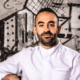 Chef Charbel Hayek wearing a white chef’s coat in front of black-and-white abstract artwork.