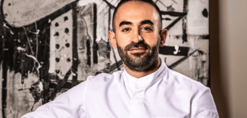 Chef Charbel Hayek wearing a white chef’s coat in front of black-and-white abstract artwork.