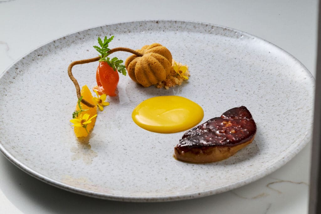 Foie gras with colorful garnishes and yellow sauce arranged on a speckled plate at COURSE in Scottsdale.