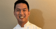 Chef Allen Rubio smiling in a white chef’s coat with his hands clasped.