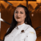 Chef Jacqueline Rojo wearing a white Ámbar chef’s coat, standing beside a staircase inside the restaurant.