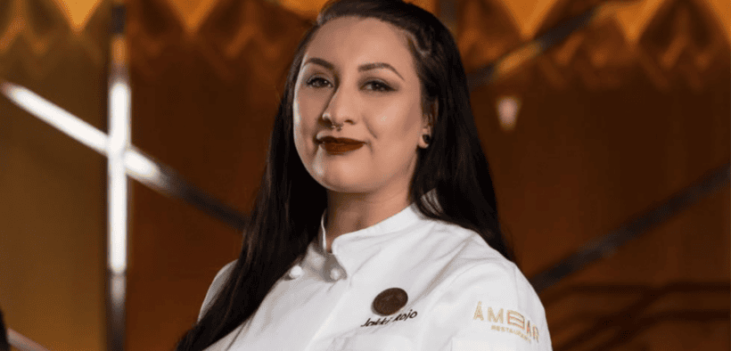Chef Jacqueline Rojo wearing a white Ámbar chef’s coat, standing beside a staircase inside the restaurant.