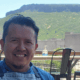 Chef Jesus Silva smiling in a blue shirt and gray apron on an outdoor patio with a mountain backdrop.