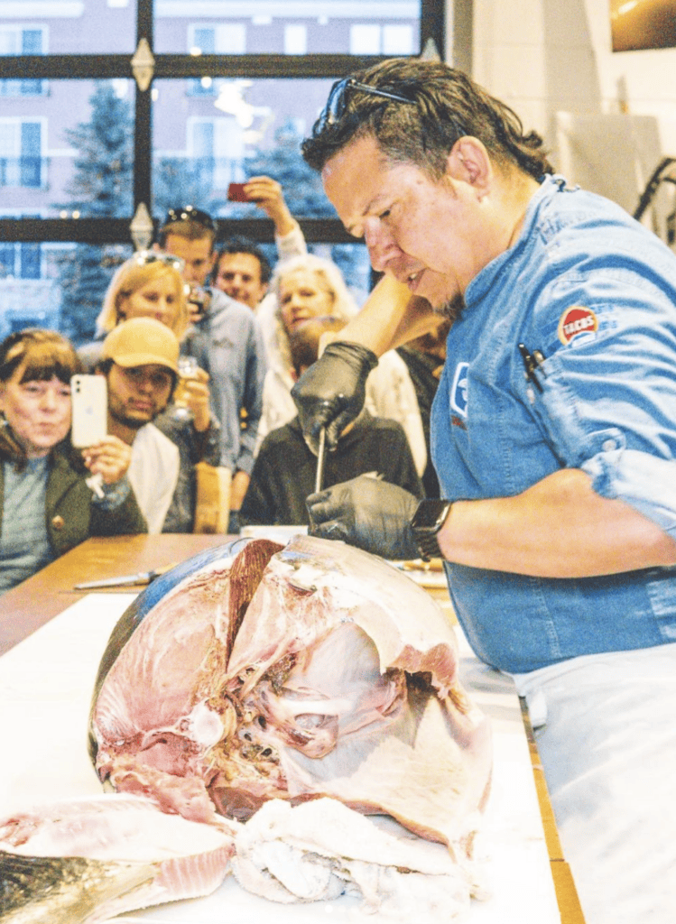 Chef Jesus Silva cutting a large tuna while a crowd watches and takes photos.