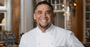 Chef Marc Quiñones smiling in a white chef’s coat inside La Plazuela in Santa Fe.