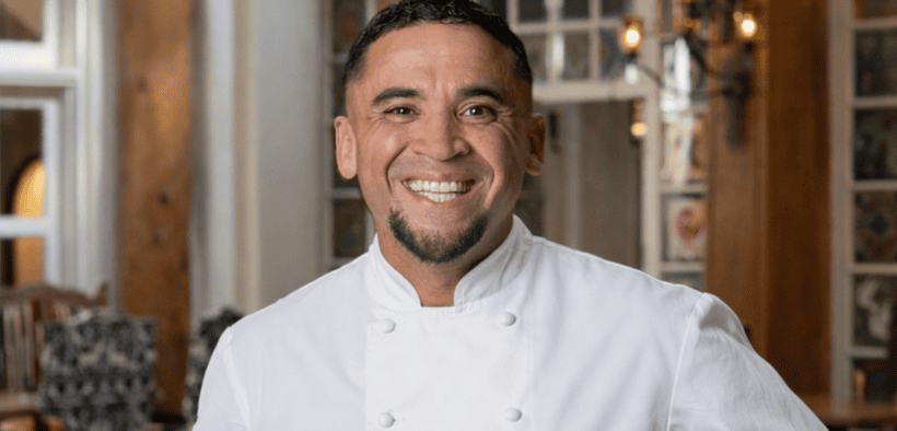 Chef Marc Quiñones smiling in a white chef’s coat inside La Plazuela in Santa Fe.