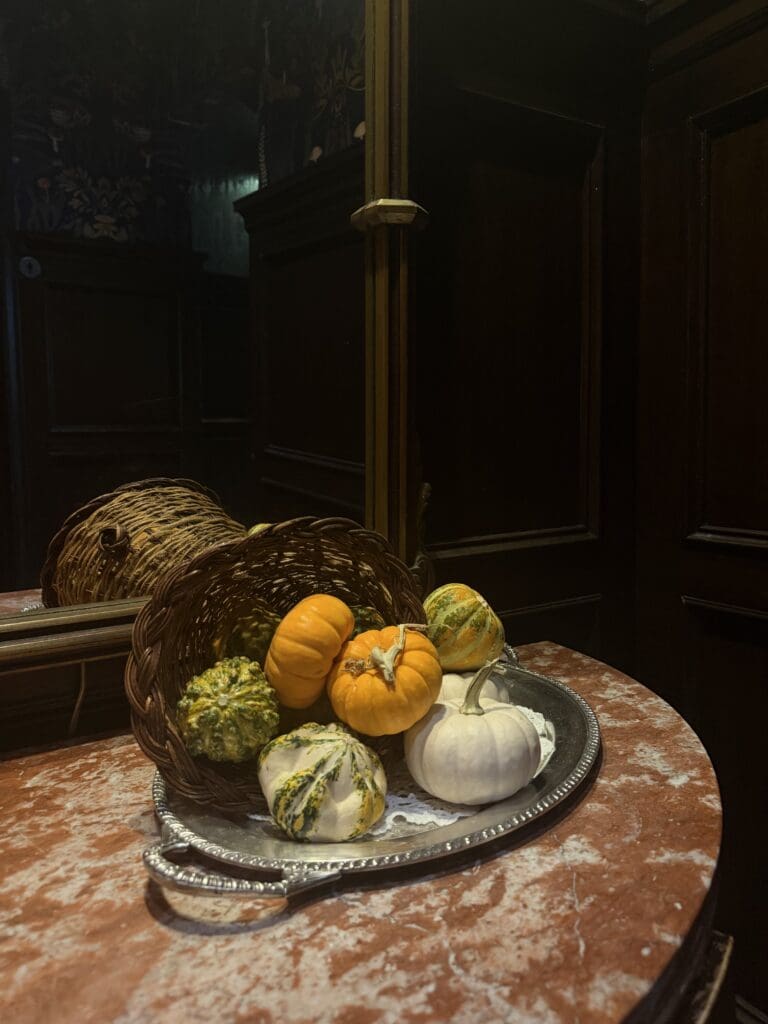 Orange, white and green gourds spill from a wicker basket onto a silver tray on a marble table at The Culver Hotel.